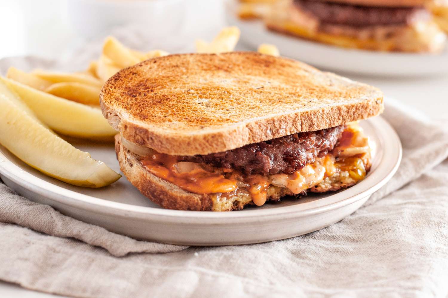 Vegan Patty Melt with Fries on a Plate over a Table Napkin, and in the Background, Another Plate with Another Serving