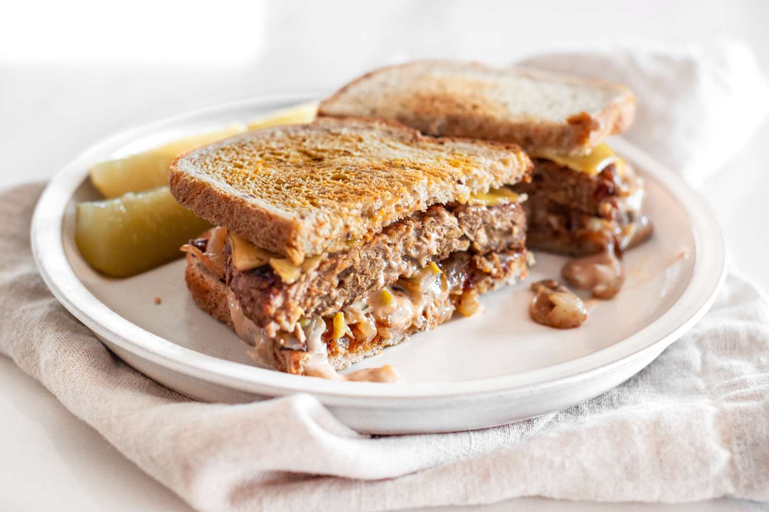 Halved Vegan Patty Melt with Pickles on a Plate over a Table Napkin