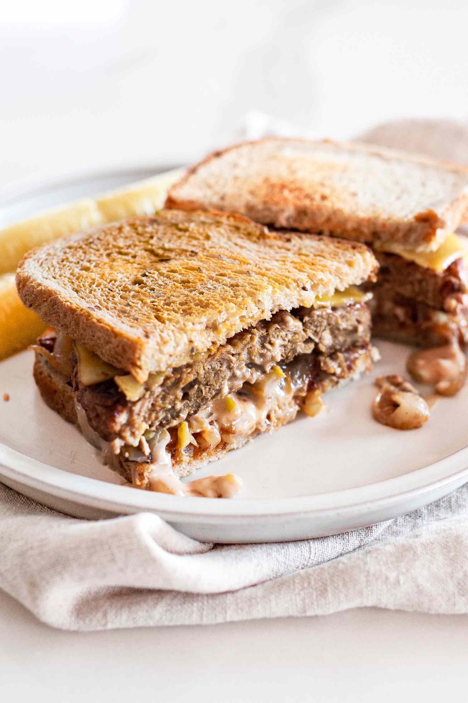 Halved Vegan Patty Melt with Pickles on a Plate over a Table Napkin