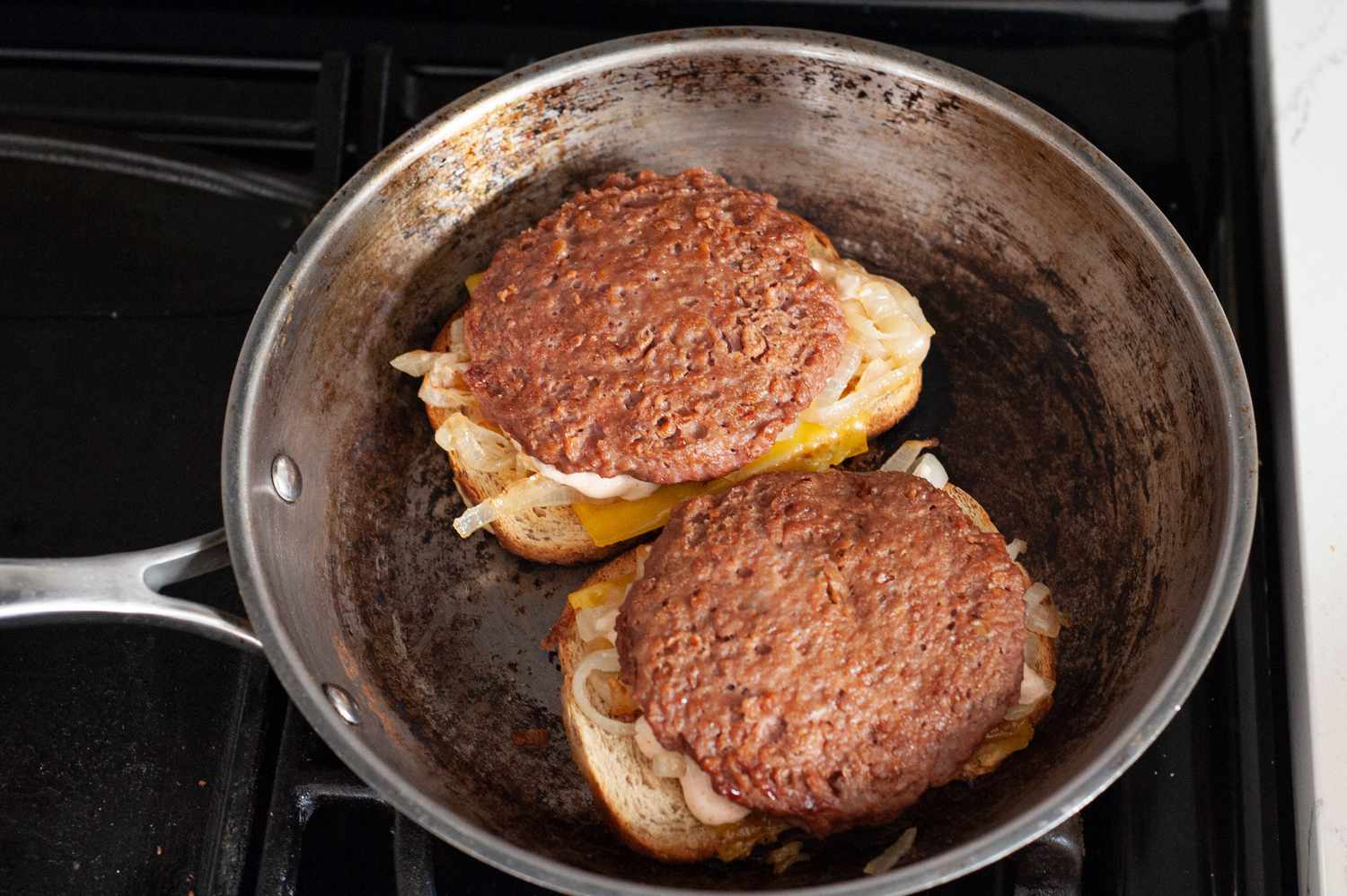 Caramelized Onions and Impossible Burger Patties Added to Sliced Bread with Cheese in Skillet for Vegan Patty Melt Recipe