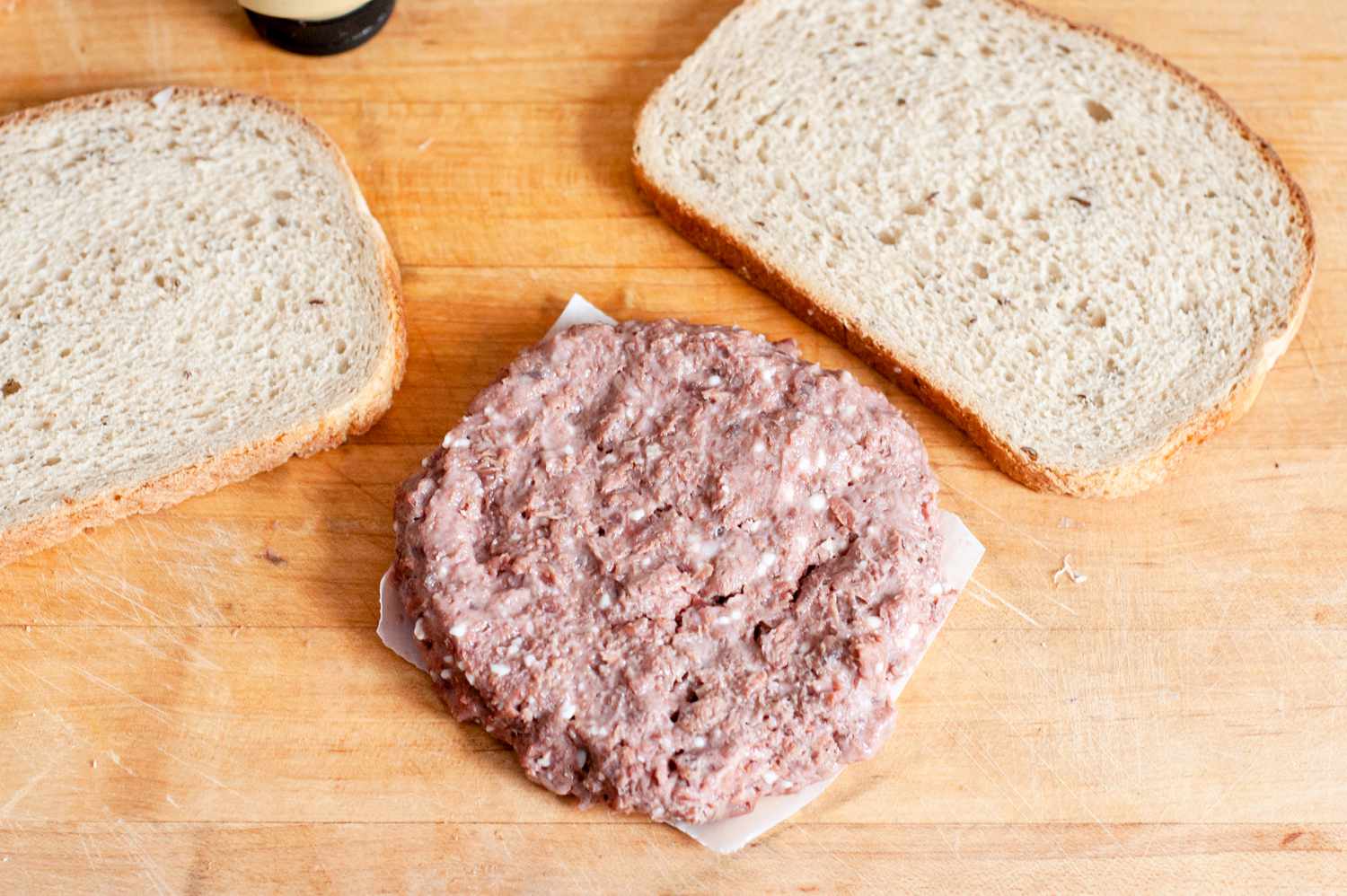 Impossible Burger on a Piece of Parchment on a Cutting Board, and Next to It, Two Slices of Rye Bread for Vegan Patty Melt Recipe