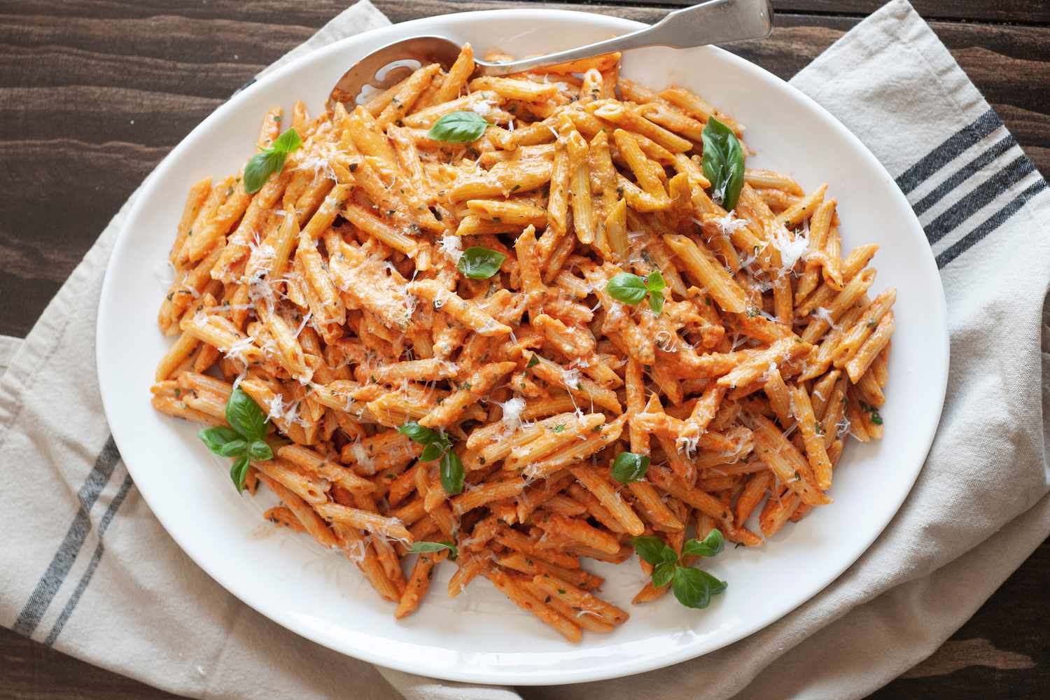 Penne alla Vodka in a Plate with a Spoon over a Kitchen Towel