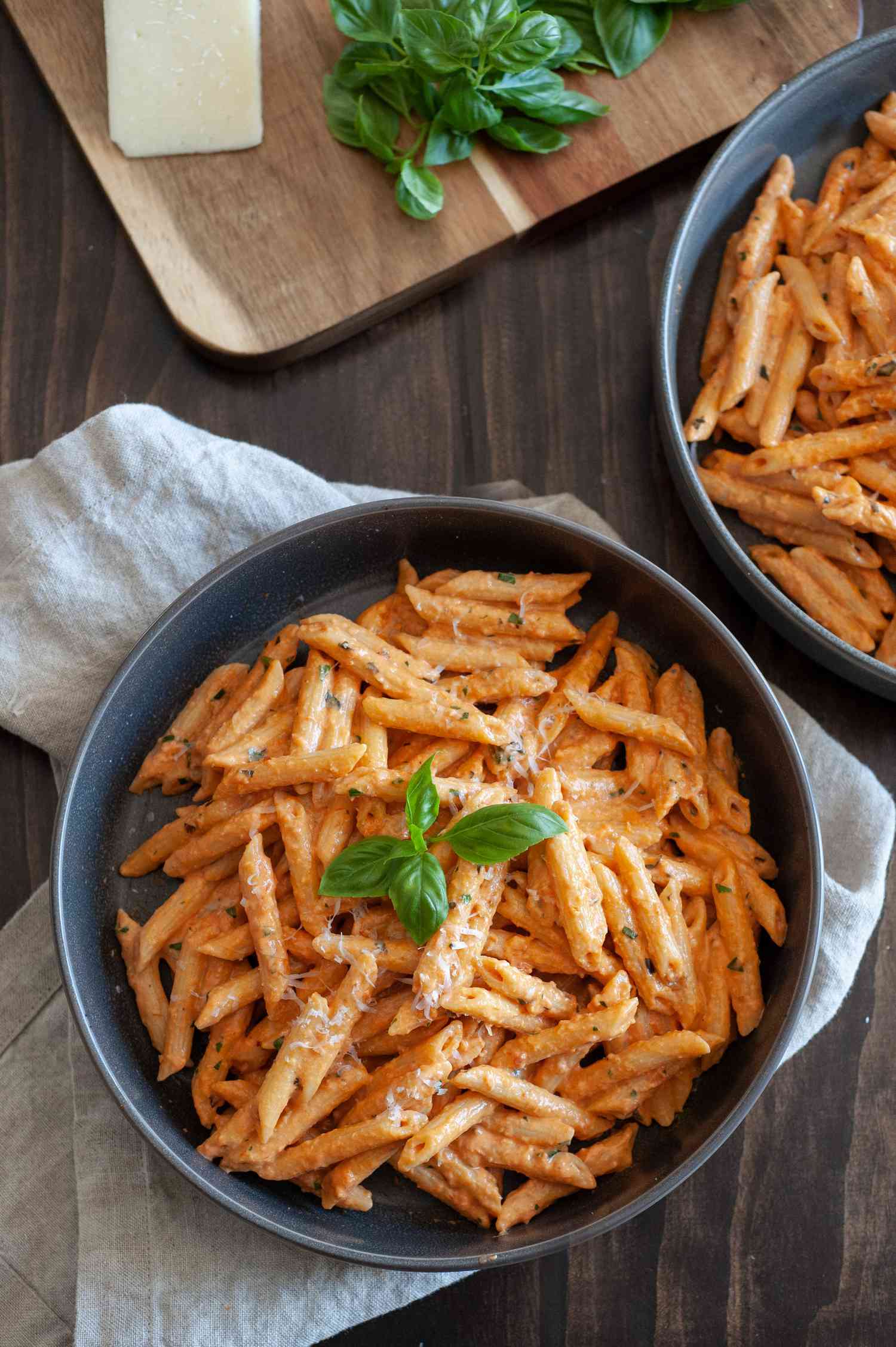 Penne alla Vodka in Two Bowls Next to a Cutting Board with Cheese and Basil