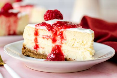 Side view of a slice of cheesecake topped with raspberry sauce.