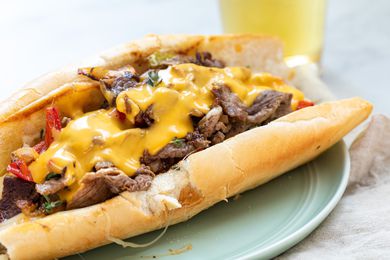 Homemade Philly Cheesesteak on a plate with a tall beer behind it.