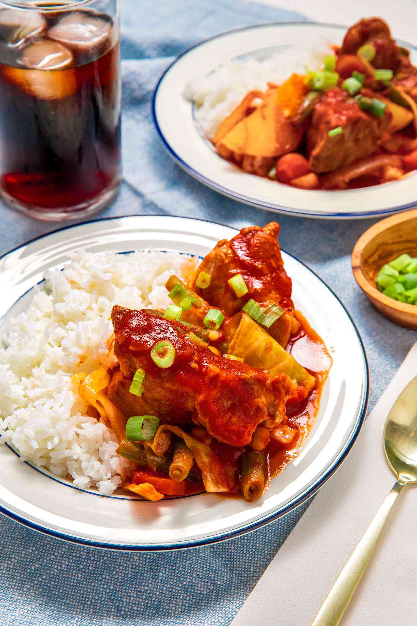 Plate of Pork Asado de Carajay With a Side of Rice, and in the Surroundings, Another Plate With the Same Serving, a Glass of Cola With Ice, and a Bowl of Sliced Green Onions