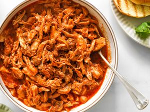 Bowl of Pulled Chicken With a Spoon Next to a Plate With a Toasted Bun and Spinach and a Light Green Table Napkin