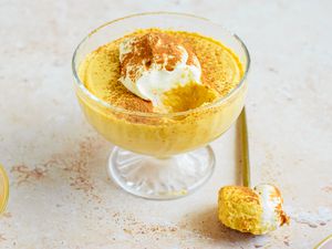 2-ingredient pumpkin mousse topped with whipped cream and a sprinkle of pumpkin spice, all in a sherbert glass. On the counter, a spoonful of mousse.