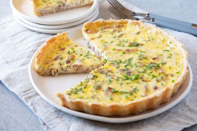 Quiche lorraine with a piece set on a plate behind it.