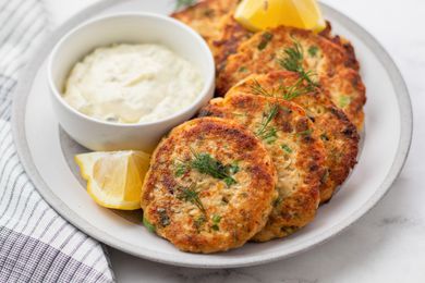 Salmon patties set on a plate with a dip and lemon.