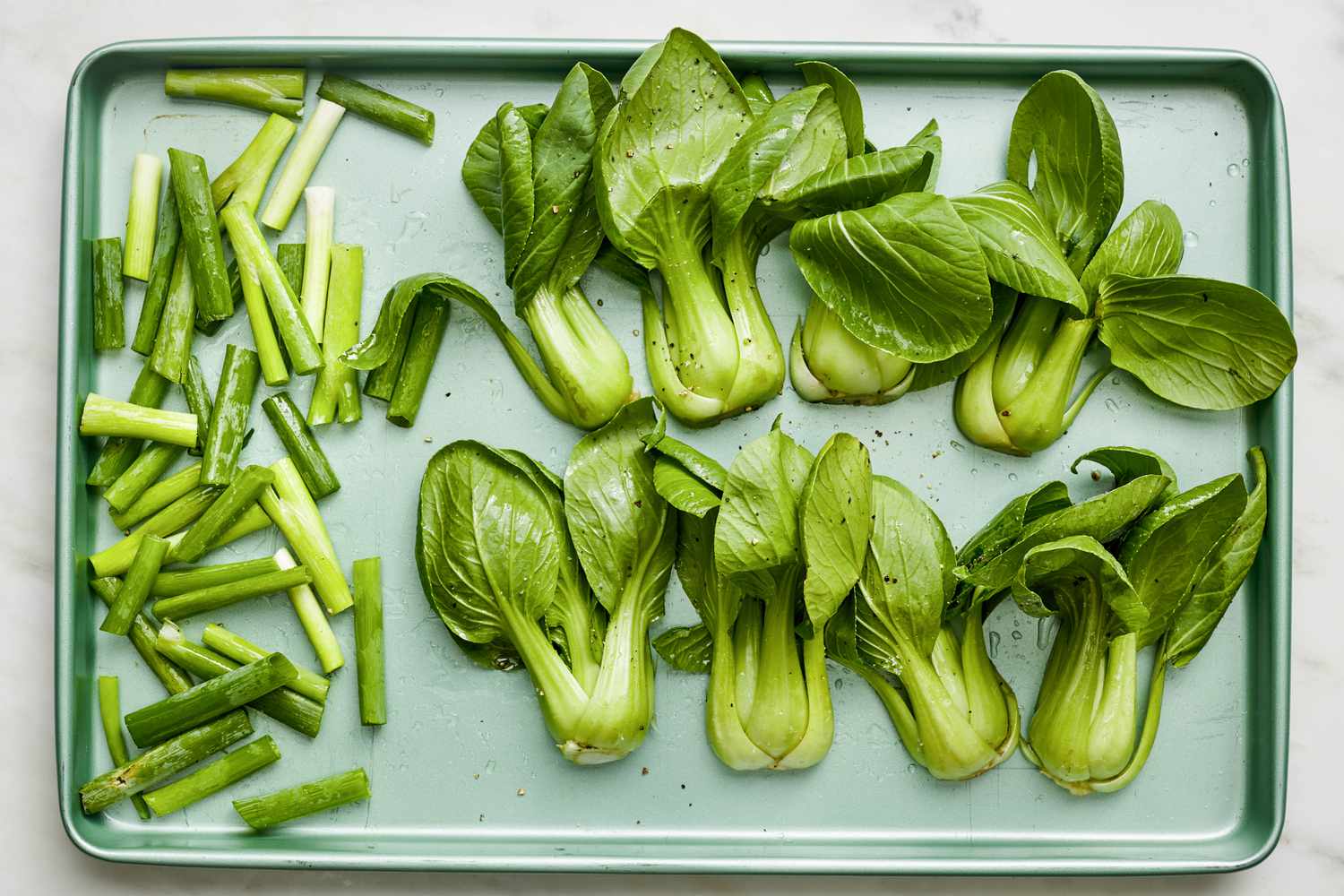 Seasoned bite sized green onions and baby bok choy on a baking sheet for 5-ingredient sheet pan teriyaki salmon recipe