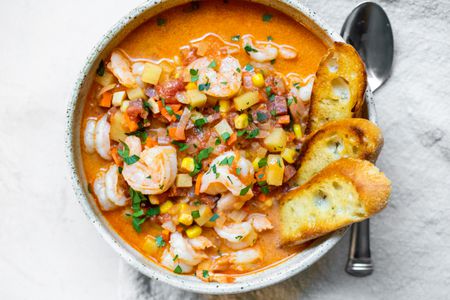 Bowl of Shrimp and Chorizo Chowder Topped with Parsley and Slices of Toasted Baguette