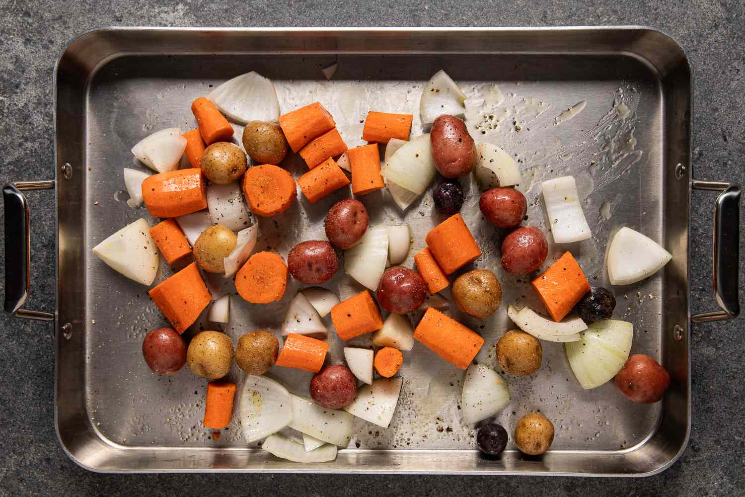 Seasoned chopped carrots, onions, and whole potatoes in a roasting pan for simple chicken roast recipe