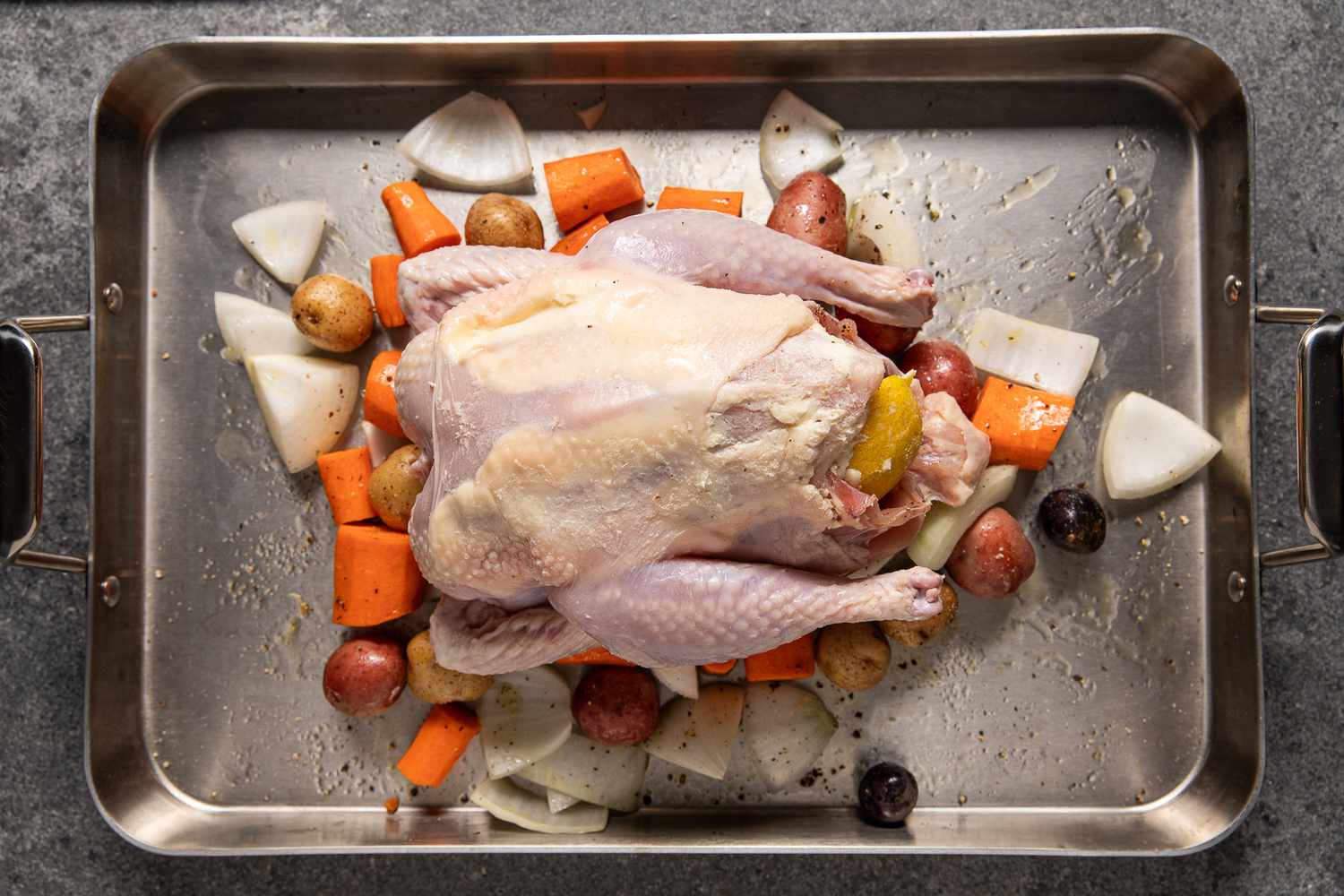 Seasoned whole chicken placed on seasoned vegetables in the roasting pan for roast chicken recipe