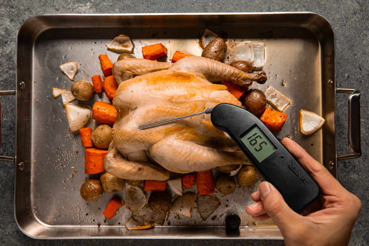 Electric thermometer checking internal temperature of the roasted chicken. Thermometer reads 165F.