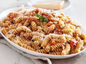 Smashed Tomato Pasta on a Serving Platter Next to a Block of Parmesan on a Plate 