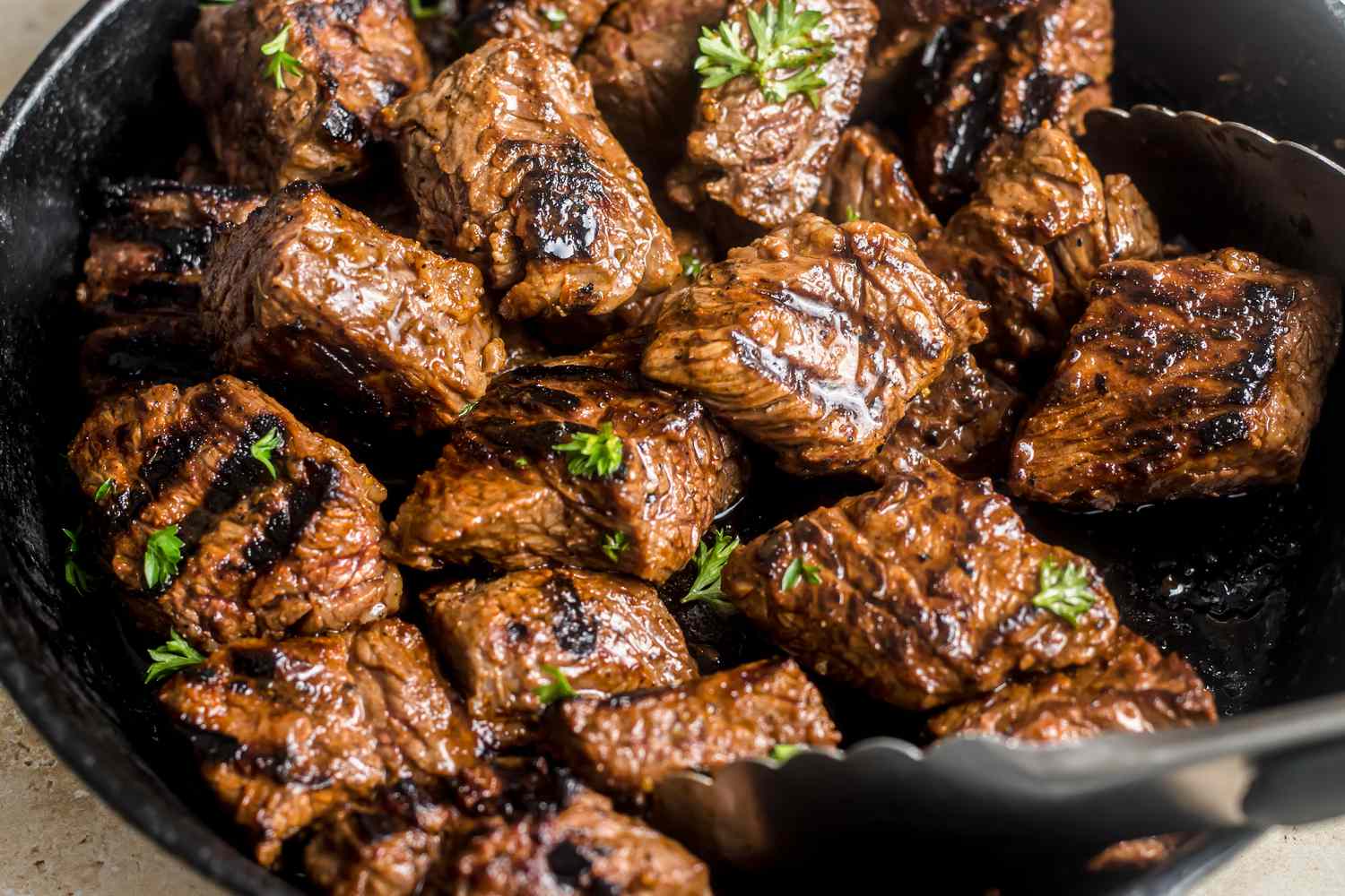 Close-up: steak tips topped with parsley on a cast iron skillet