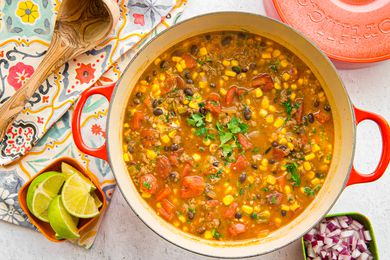 Stovetop Taco Soup in a Dutch Oven Surrounded by Bowls of Sour Cream, Diced Red Onions, and Lime Wedges