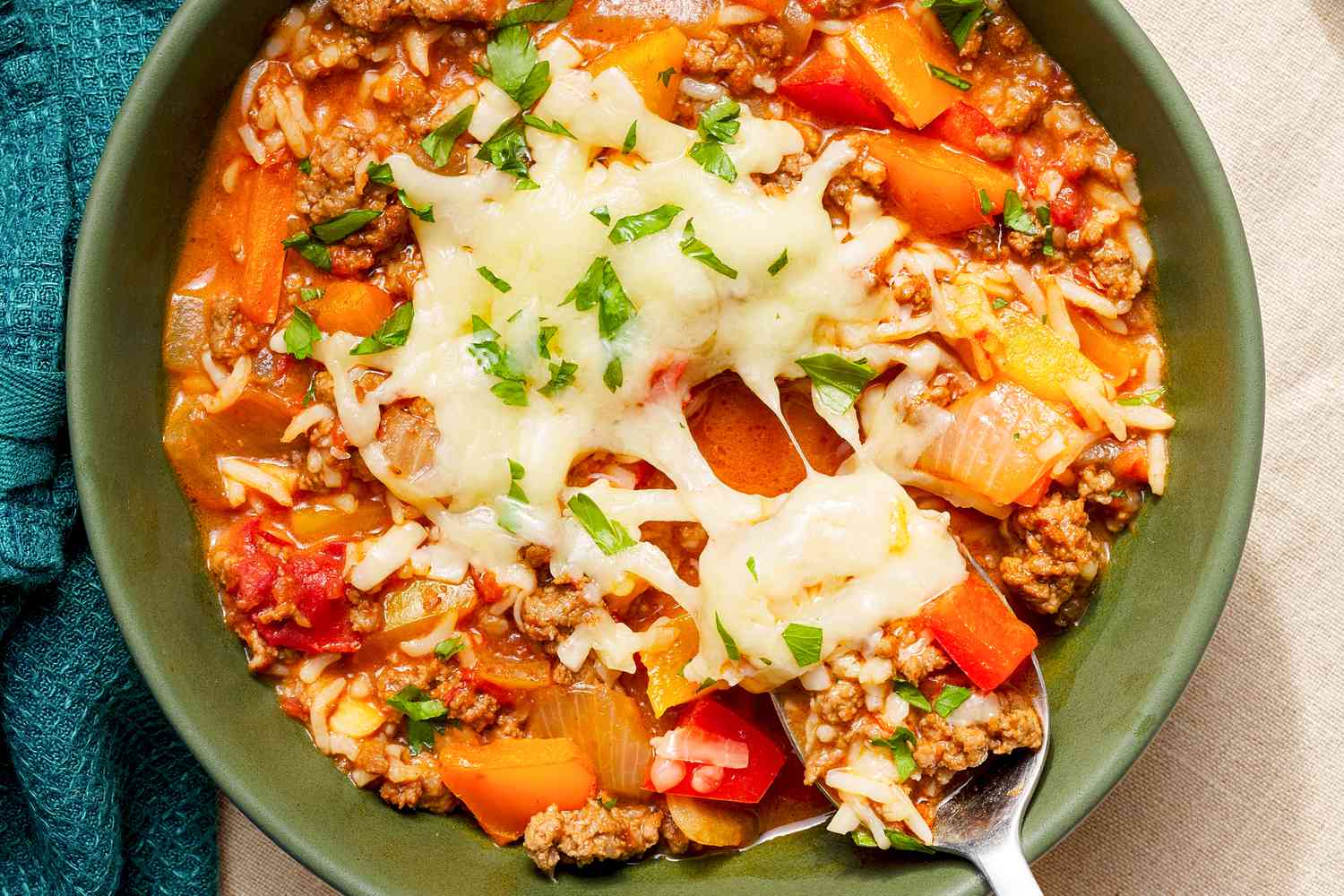 Bowl of stuffed pepper soup topped with cheese and some of the soup in a spoon being taken from the bowl