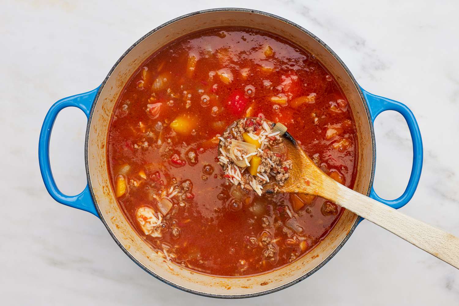 Wooden spoon lifting rice, ground beef, and sauteed vegetables from stuffed pepper soup in the dutch oven 