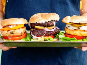 Person holding a tray of three burgers. 