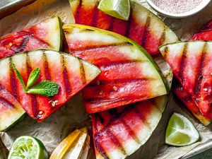 Triangles of grilled watermelon with small bowl of spice mix, sprig of mint and lime wedges alongside