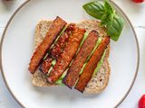 Overhead view of vegetarian bacon on a piece of bread with avocado underneath it.