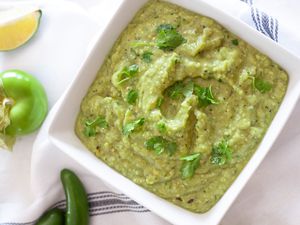 Bowl of Tomatillo Avocado Salsa Surrounded by Tomatillos, Lime Wedges, and Jalapeños