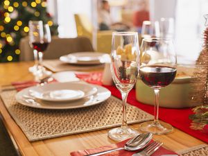 A festive dinner table set with wine glasses and plates with a Christmas tree in the background