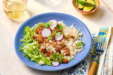 Plate of 5-ingredient turkey taco bowl at a table setting with a glass of water, bowl of lime wedges, and a fork on a table napkin