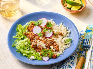 Plate of 5-ingredient turkey taco bowl at a table setting with a glass of water, bowl of lime wedges, and a fork on a table napkin