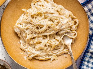 Bowl of Vegan Fettucine Alfredo With a Fork and Surrounded by a Blue and White Checkered Table Napkin and a Glass of Wine