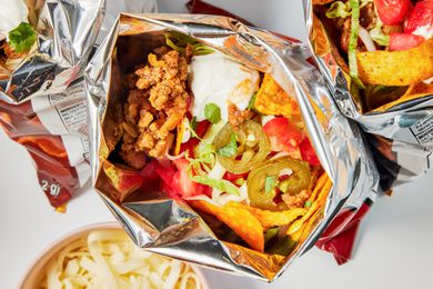 Bags of walking tacos with toppings on the counter next to a bowl of shredded mozzarella