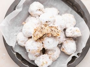 Overhead view of powdered sugar cookies piled on a plate with the top one cut in half to show the interior.