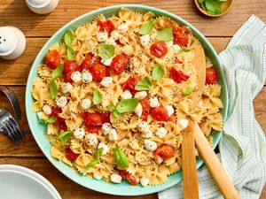 Bowl of 5-ingredient warm caprese pasta at a table setting with a table napkin, salt and pepper shaker, a small bowl of basil, and a stack of plates