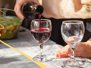 Pouring red wine into a glass on a tableclothed table outside