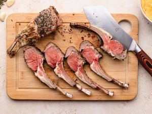 Rack of lamb cut into chops on cutting board with a knife