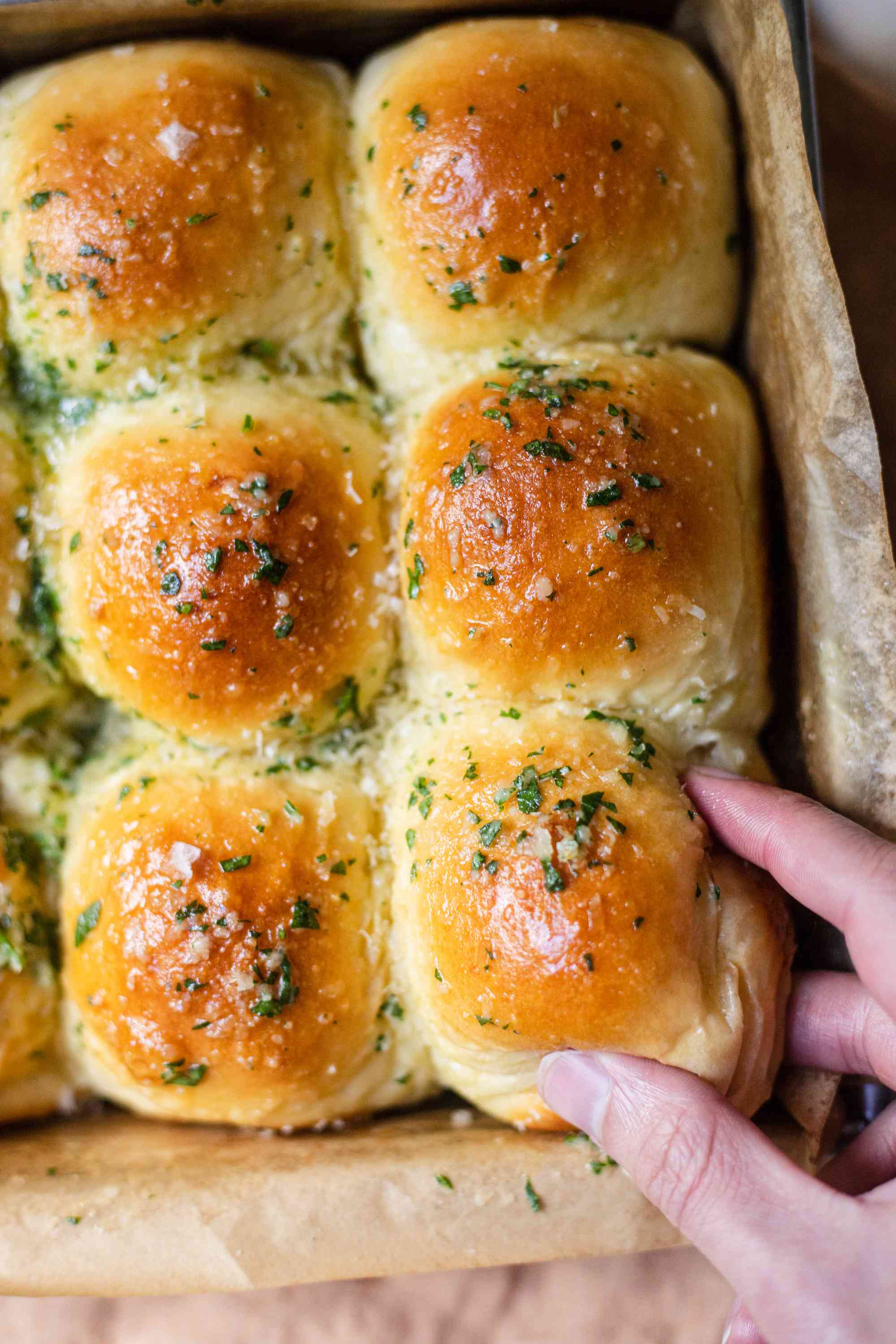 A hand grabbing a pull apart rolls with garlic and parmesan out of a pan.