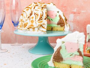 Baked Alaska with Slices Missing on a Cake Stand, and in the Surroundings, Two Plates with Slices of Baked Alaska and Champagne Flutes