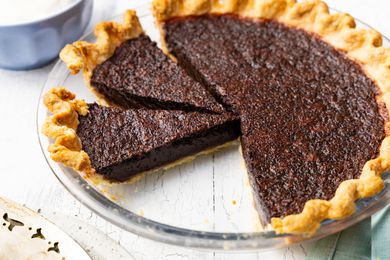 Chocolate Chess Pie With Some Cut Into Slices in a Pie Dish, and in the Surroundings, a Pie Server and a Bowl With Whipped Cream