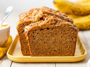 Spiced Dulce de Leche Banana Bread (Some of It Sliced) on a Platter, and in the Surroundings, a Bowl With More Dulce de Leche and Bananas