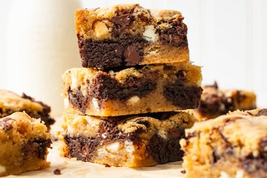 Stack of slices of marble brownies on a piece of parchment paper, and on the counter surrounding the stack, a carafe of milk and more slices of the brownies