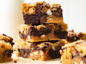 Stack of slices of marble brownies on a piece of parchment paper, and on the counter surrounding the stack, a carafe of milk and more slices of the brownies