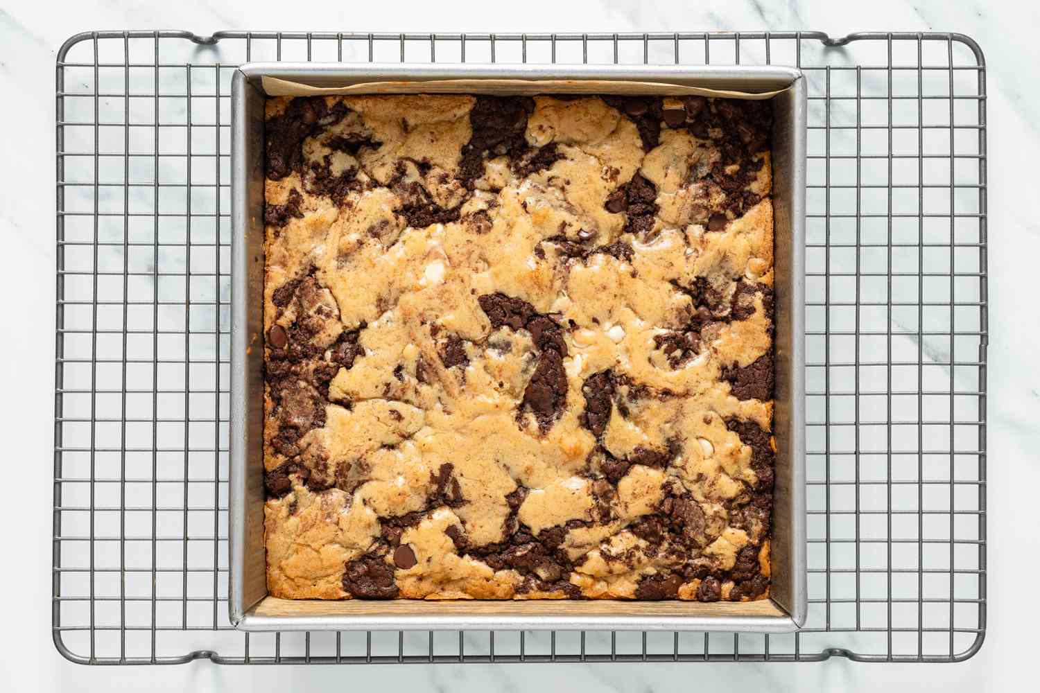 Baked marble brownies in the lined square baking pan cooling on a wire rack