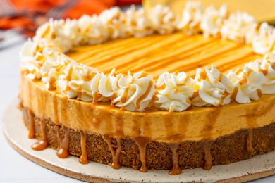 Close-up: No-bake pumpkin cheesecake on a platter, and in the background, a stack of plates, utensils on the counter, and an orange kitchen towel