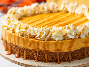 Close-up: No-bake pumpkin cheesecake on a platter, and in the background, a stack of plates, utensils on the counter, and an orange kitchen towel