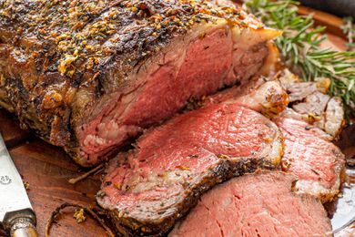 Prime rib with cut slices cascading onto the wooden platter (next to a sprig of rosemary and the carving knife)