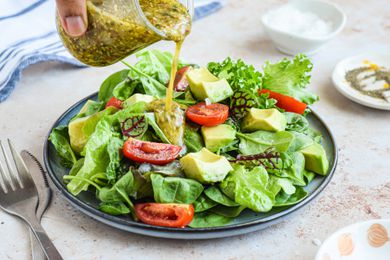 Jar of Tarragon-Mustard Vinaigrette Poured onto a Salad (Various Lettuce Types, Sliced Tomatoes, and Sliced Avocado)